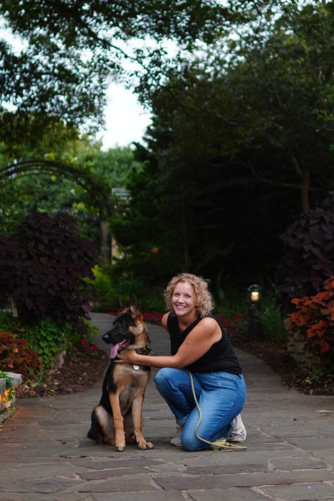 Woman kneeling on a stone path with a dog in a garden setting